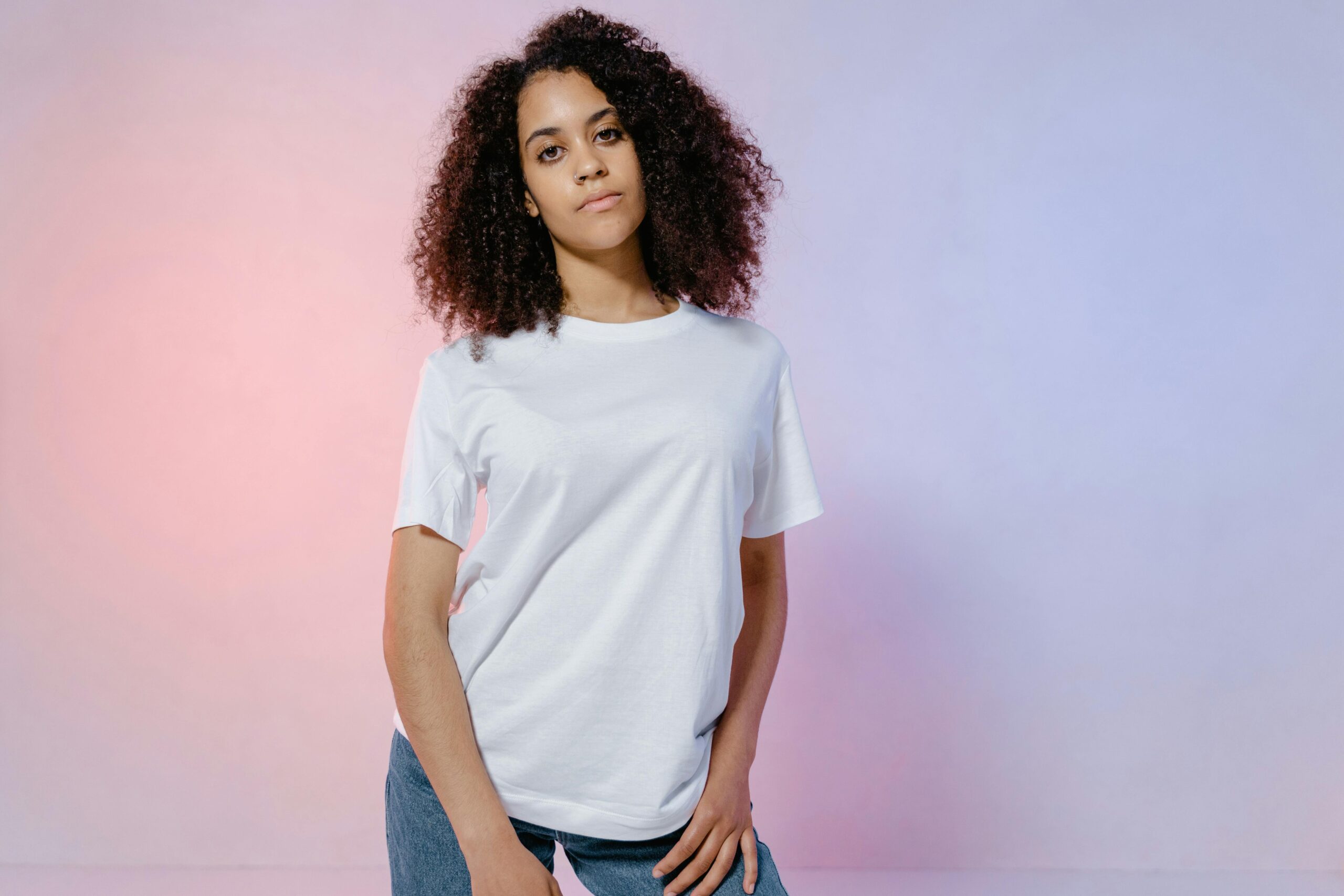 Portrait of a confident woman with curly hair in a casual white t-shirt against a soft color background.